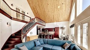 Ein geräumiger Wohnbereich mit einem großen, blauen Ecksofa, einer Holztreppe und einer Küche im Hintergrund.