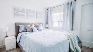 Ein Schlafzimmer mit Bett, Nachttisch und einem Fenster mit Vorhängen.