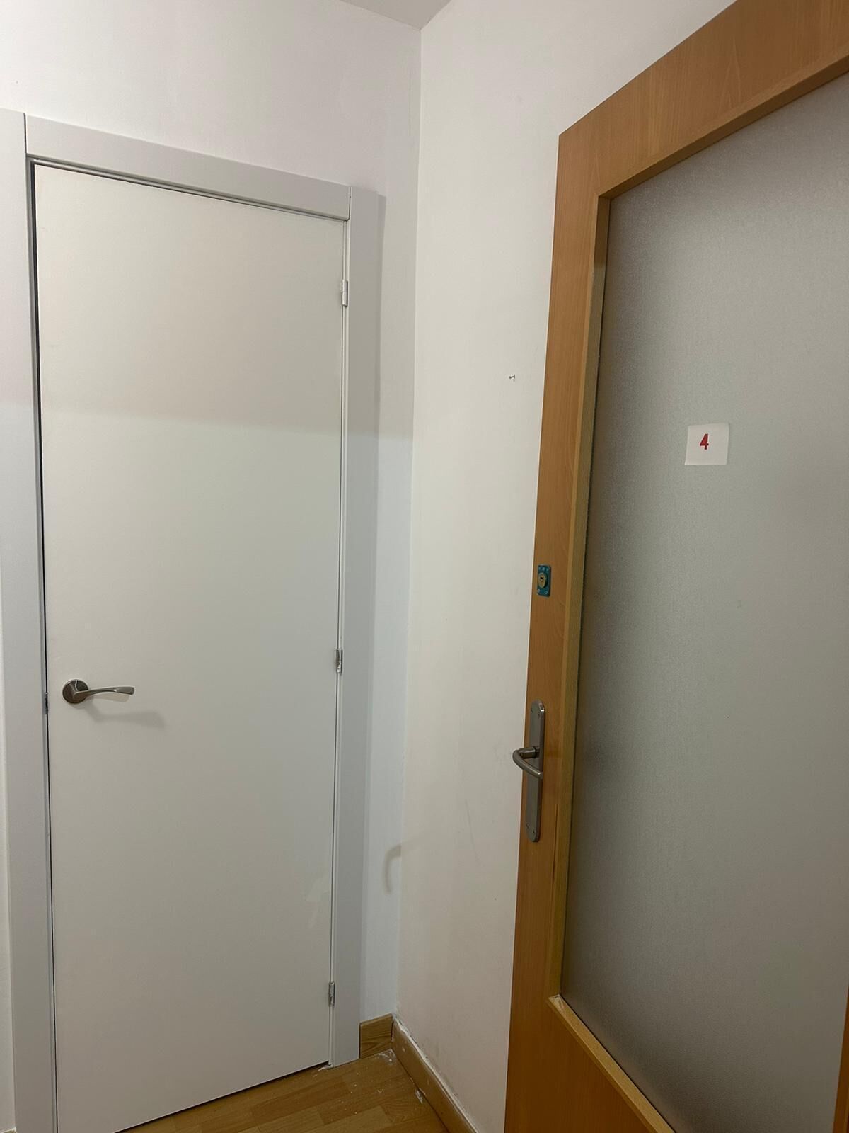 Un pasillo con una puerta blanca a la izquierda y una puerta de madera con un panel de vidrio satinado a la derecha.