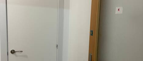 Un pasillo con una puerta blanca a la izquierda y una puerta de madera con un panel de vidrio satinado a la derecha.