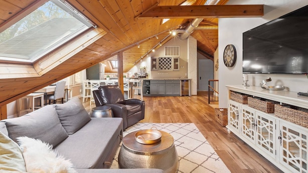Un acogedor espacio tipo loft con techo alto, vigas de madera, tragaluces, cocina moderna y zona de estar confortable.