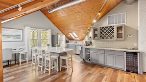 Una cocina moderna con vigas de madera, un comedor con mobiliario blanco y un amplio ventanal con vistas.