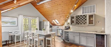 Una cocina moderna con vigas de madera, un comedor con mobiliario blanco y un amplio ventanal con vistas.