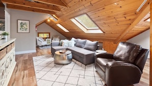 Una sala de estar estilo loft acogedora, con techo inclinado, vigas de madera y tragaluces.
