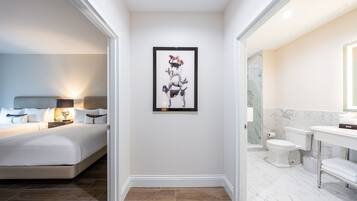 A modern hotel room with a bed, a framed artwork on the wall, a bathroom with a toilet, sink, and mirror.