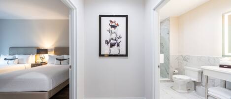 Una habitación de hotel moderna con una cama, una obra de arte enmarcada en la pared, y un baño con inodoro, lavamanos y espejo.
