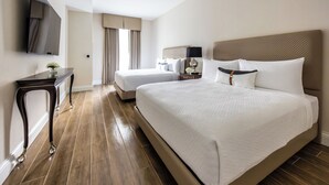 A hotel room with a large bed, a smaller bed, a desk, a flat-screen TV, and a window with curtains.