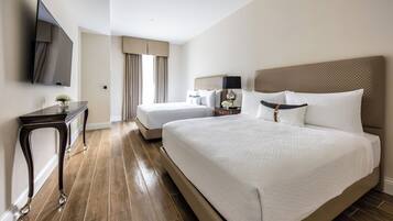 A hotel room with a large bed, a smaller bed, a desk, a flat-screen TV, and a window with curtains.