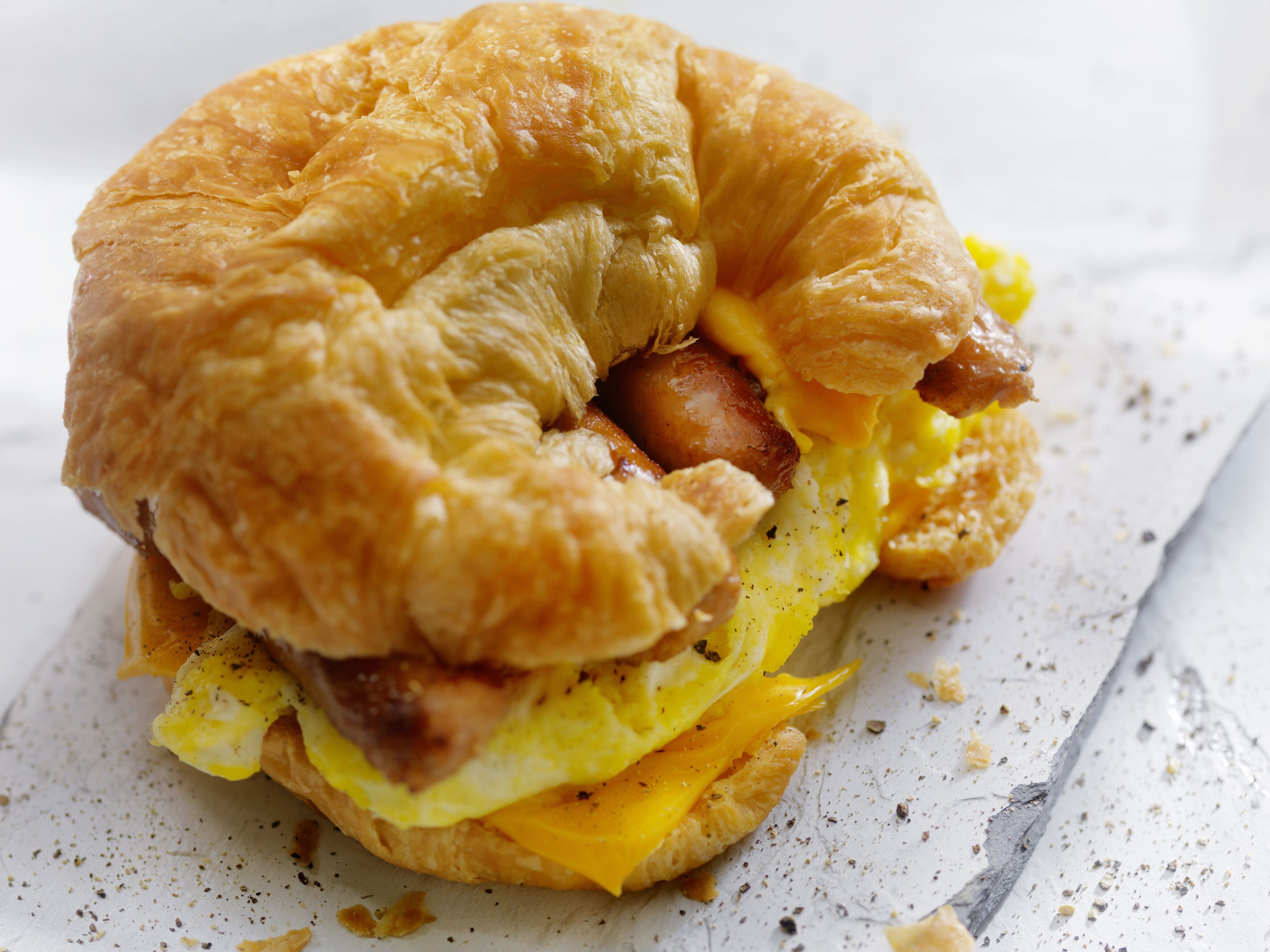 A breakfast sandwich with eggs, cheese, and sausage in a croissant.