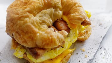 Sanduíche de café da manhã com ovos, queijo e salsicha em um croissant.
