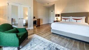 A hotel room with a large bed, a green armchair, a white rug, and wooden flooring.