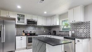 A modern kitchen with white cabinets, a granite countertop, stainless steel appliances, and a patterned backsplash. - Bright and Stylish Home (Dallas)