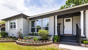 A two-story house with a stone facade, large windows, a front porch with steps, and a well-maintained garden. - Bright and Stylish Home (Dallas)
