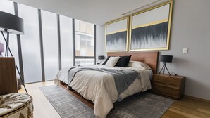 Une chambre à coucher moderne avec un grand lit, une table de chevet en bois, deux lampes de chevet et une grande fenêtre avec des stores.