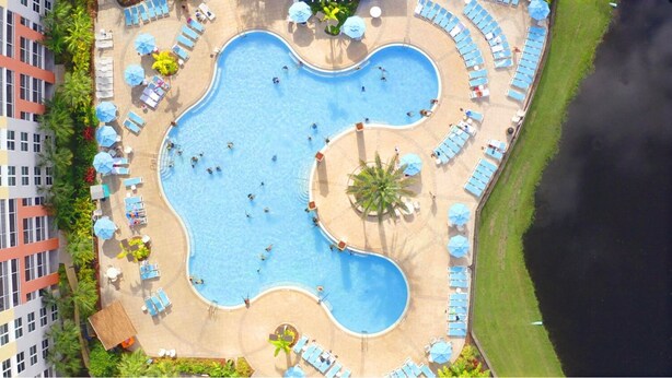 Eine Vogelperspektive auf einen Hotelpoolbereich mit mehreren Schwimmbecken, Liegestühlen und Sonnenschirmen.