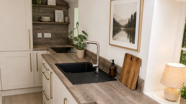 Una cocina moderna con armarios blancos, una encimera de madera, un lavabo negro, una tabla de cortar de madera, un cuadro enmarcado y una lámpara.