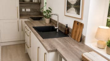 Une cuisine moderne avec des meubles blancs, un plan de travail en bois, un évier noir, une planche à découper en bois, un tableau encadré et une lampe.