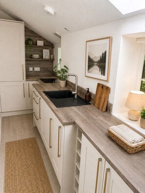 A modern kitchen with white cabinetry, a wooden countertop, a black sink, a wooden cutting board, a framed picture, and a lamp.