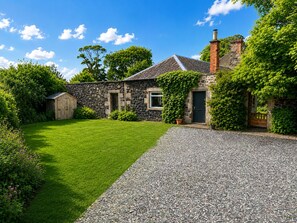 A stone house with a gravel driveway, a wooden shed, and a well-maintained lawn.