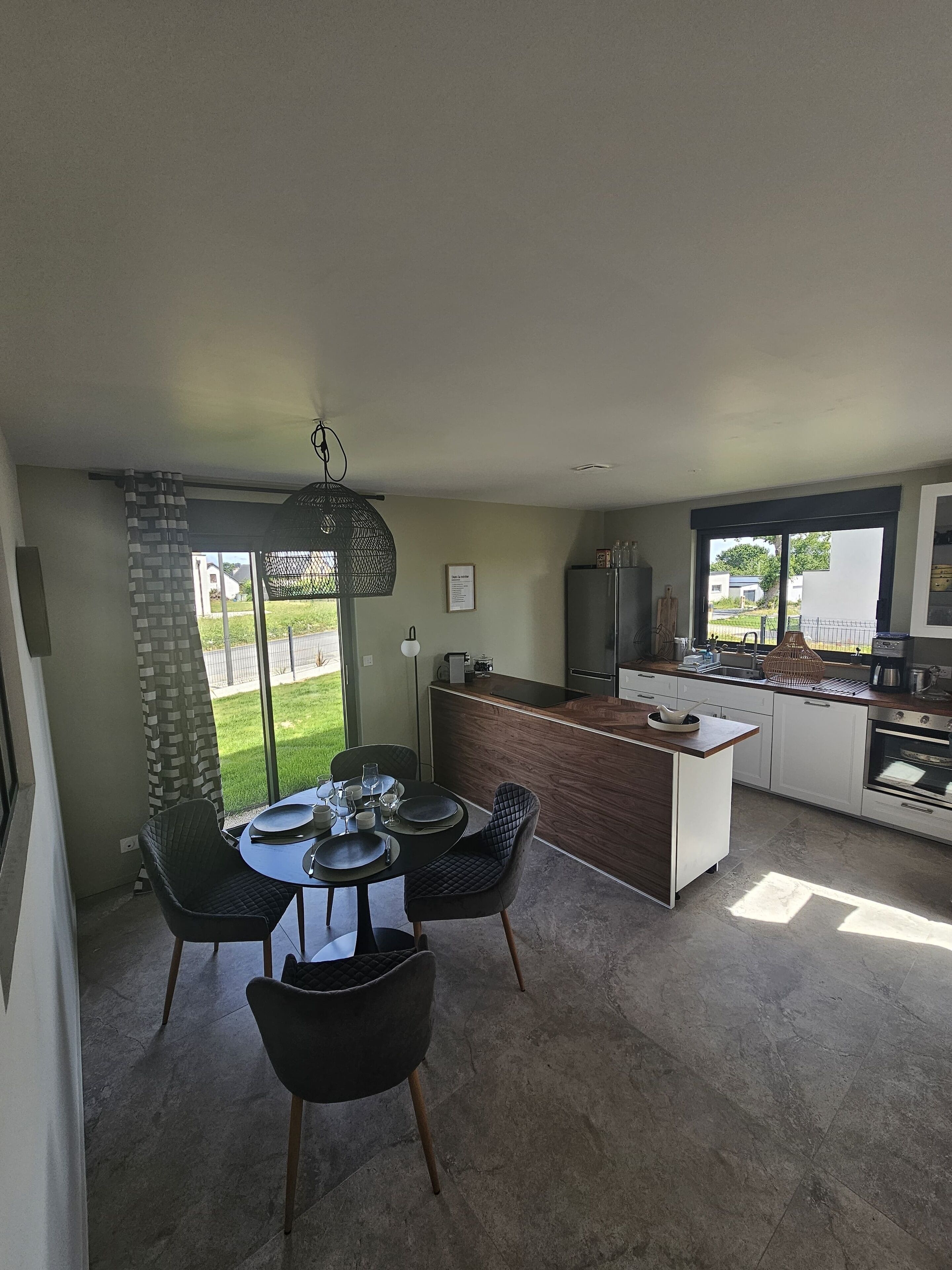 Een moderne keuken met een centraal eiland, een zithoek met twee stoelen, en een grote schuifpui naar een tuin.