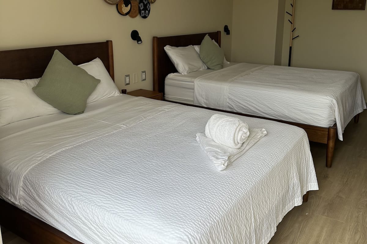 Two single beds with wooden frames and white bedding, a wall-mounted hat rack, and a wooden floor.