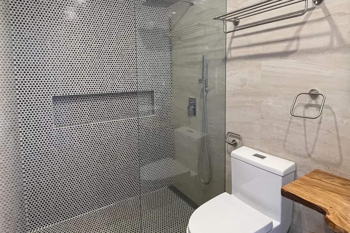 A modern bathroom with a glass-enclosed shower, a white toilet, and a wooden shelf.