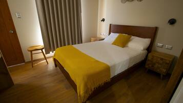 A bedroom with a wooden bed, a yellow throw blanket, a wooden nightstand, and a small stool.