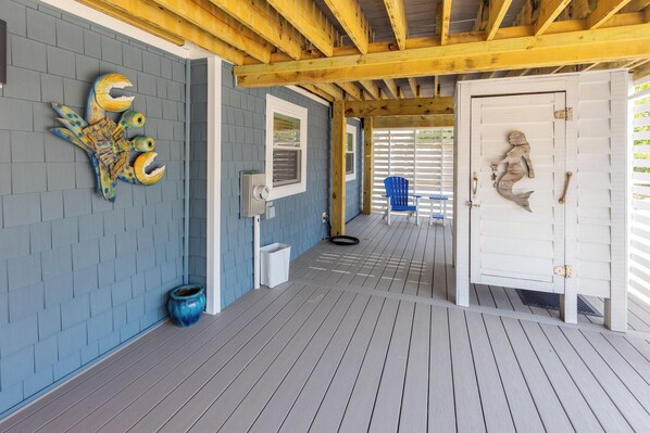 A covered outdoor area with a wooden ceiling, a blue wall with a decorative fish sculpture, a white door with a mermaid cutout, and a blue chair.