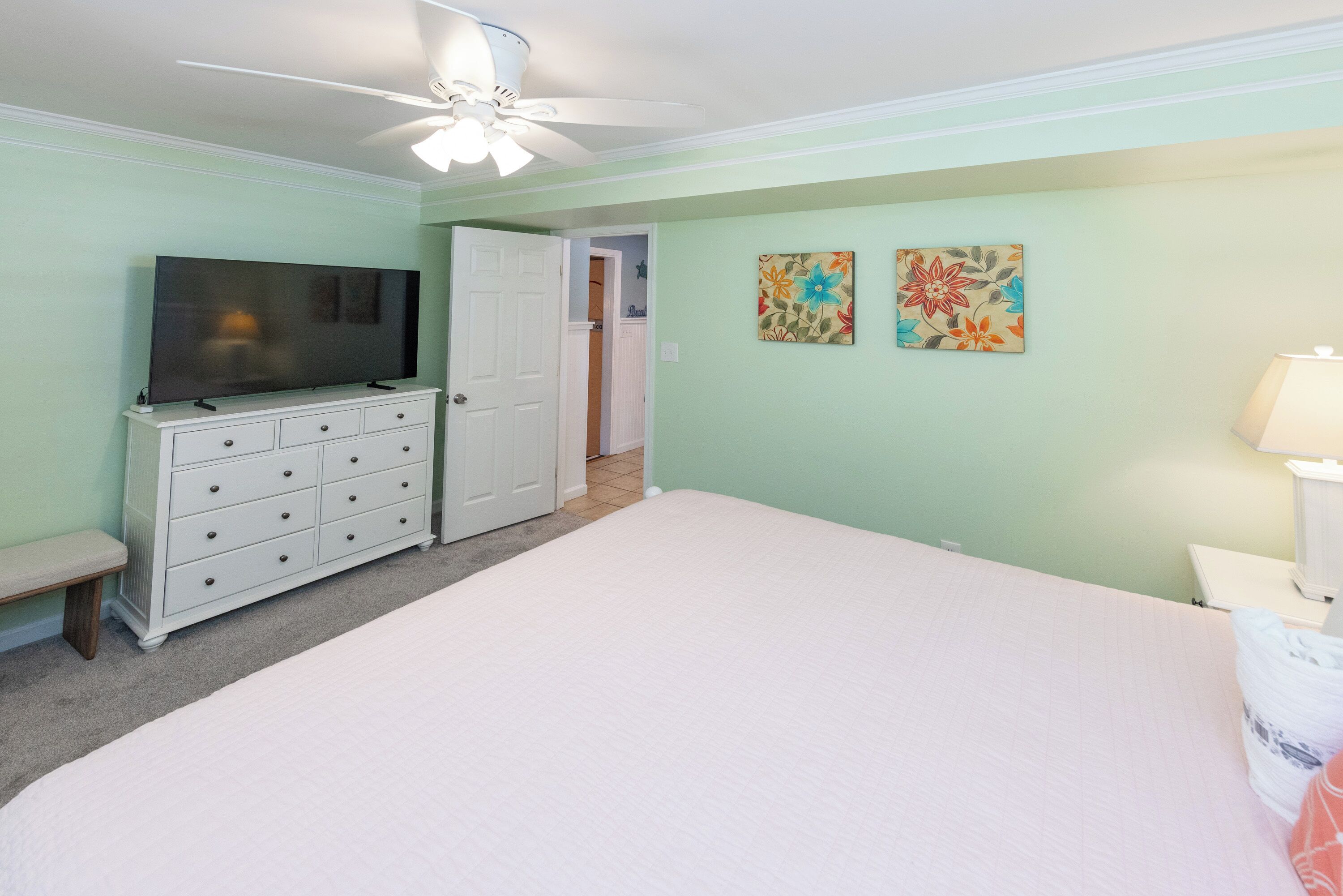 A bedroom with a bed, a dresser, a television, and two wall-mounted paintings.