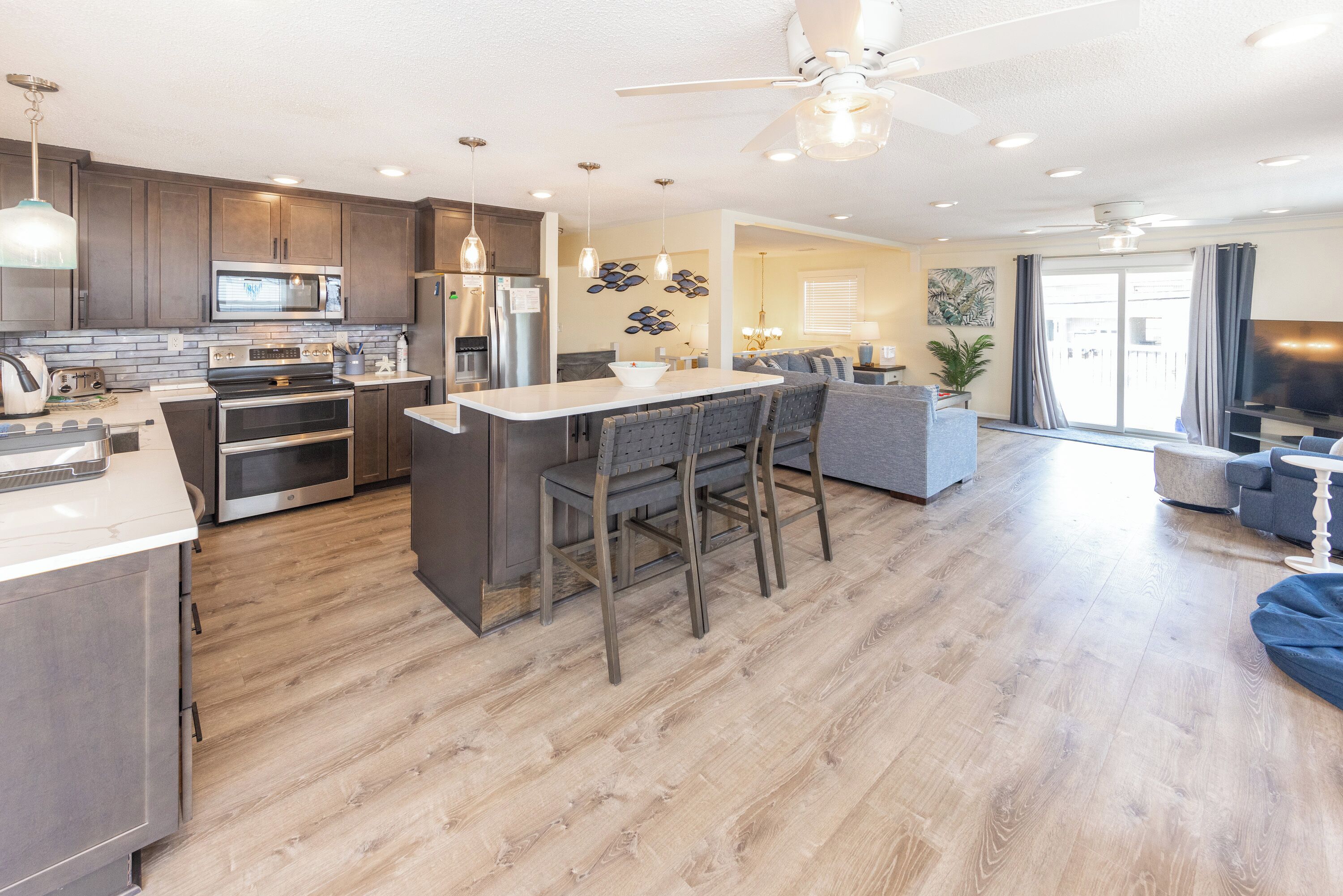Una cocina moderna con una isla central, un comedor con un taburete de bar y una sala de estar con sofá y televisor.