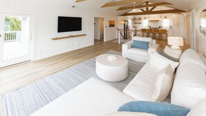Un salon spacieux avec un canapé blanc, une table basse ronde et un téléviseur à écran plat fixé au mur.