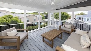Une terrasse extérieure couverte, dotée de meubles en bois et d’une rambarde blanche.