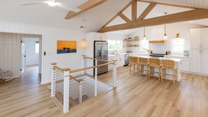 Une cuisine spacieuse avec des meubles blancs, un plafond en bois et un îlot central doté de tabourets de bar.