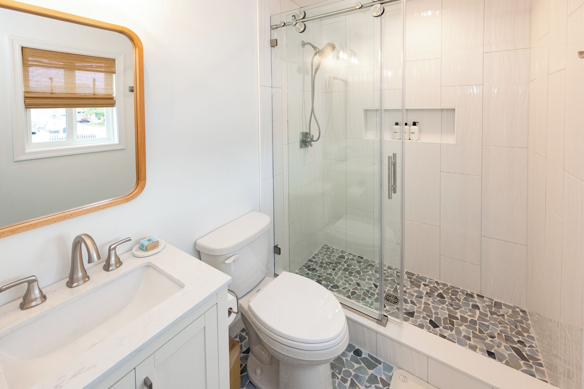 Un baño moderno con cabina de ducha de vidrio, inodoro blanco y lavamanos de mármol.