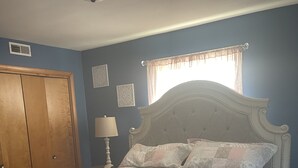 Une chambre à coucher avec un grand lit, une armoire en bois, une table de chevet avec une lampe et une fenêtre ornée de rideaux légers.