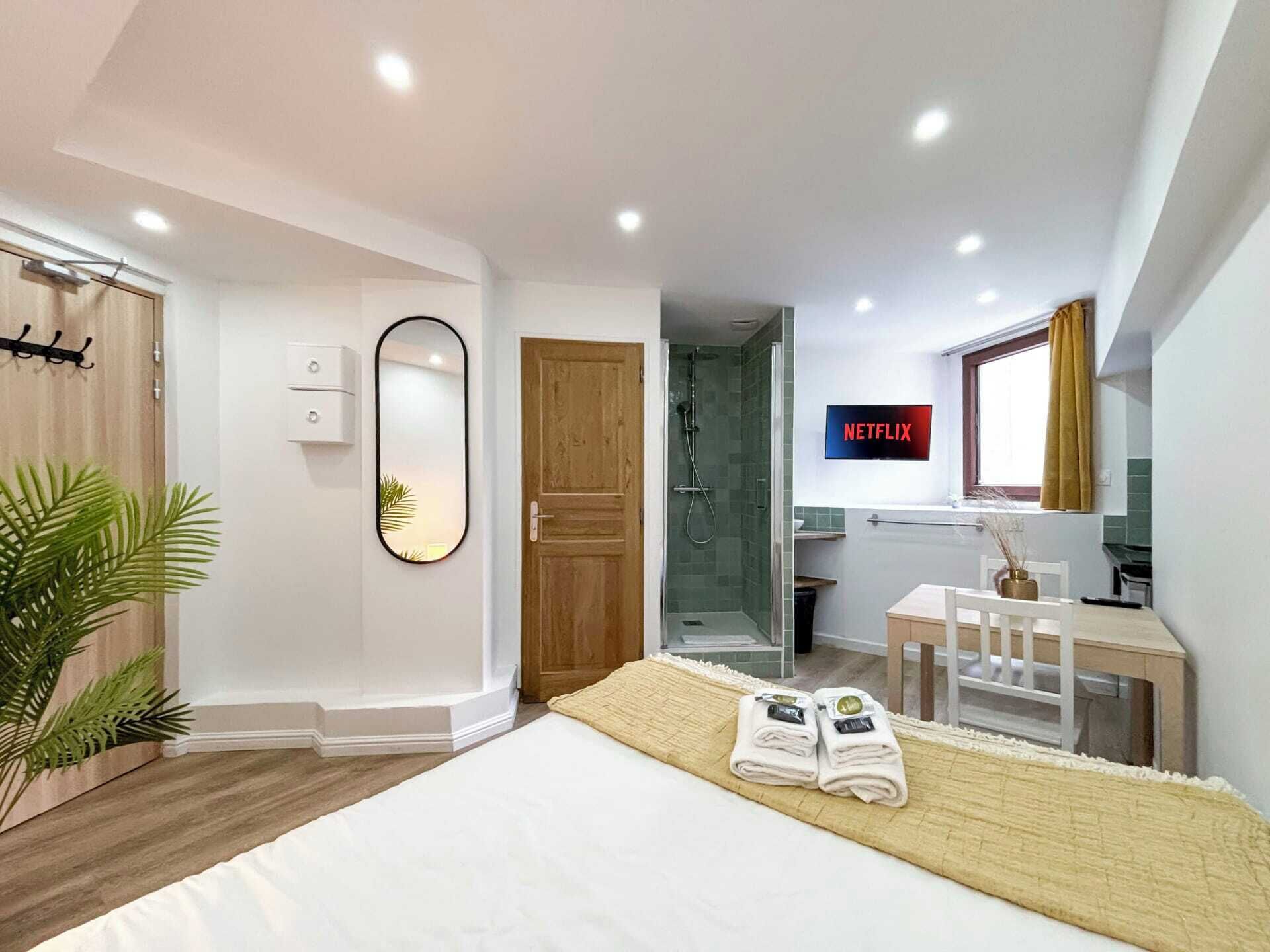 Ein modernes Hotelzimmer mit Bett, Dusche, Fernseher und Schreibtisch mit Stuhl.