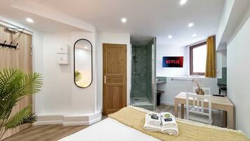 Ein modernes Hotelzimmer mit Bett, Dusche, Fernseher und Schreibtisch mit Stuhl.