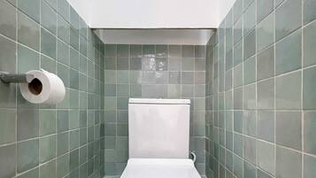 Ein kleines Badezimmer mit Toilette, Toilettenpapierhalter und Warmwasserbereiter.