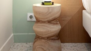 Eine Ecke eines Zimmers mit einem Nachttisch aus Holz, einer Lampe, einer Steckdose und einem Bett.