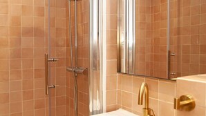 Ein modernes Badezimmer mit einer Duschkabine, einem weißen Waschbecken mit goldenen Armaturen und einem großen Spiegel.