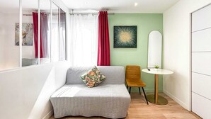 Een moderne slaapkamer met een grijze bank, een klein rond tafeltje en een spiegel.