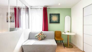 Un dormitorio moderno con un sofá gris, una mesita redonda y un espejo.