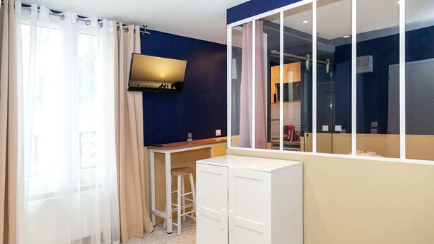 A compact room with a bed, a small table with a plant, a TV mounted on the wall, and a window with curtains. - David D Angers 53 - One Bedroom Apartment, Sleeps 4 (Paris)