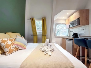 A bedroom with a bed, pillows, a bedside table, and a window with curtains.