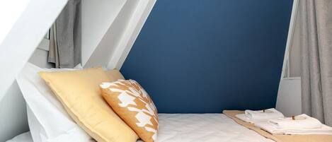Ein kompakter, dreieckiger Raum mit einem Bett, Kissen und einer hölzernen Bank.