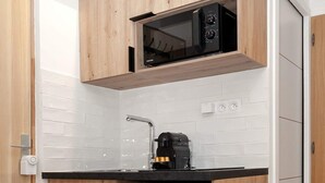 Una cocina compacta con armarios de madera, un refrigerador de acero inoxidable, un microondas negro y una cafetera.