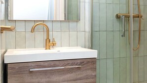 Un baño con lavamanos blanco, tocador de madera, un espejo grande y cabina de ducha con paredes de vidrio.