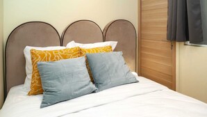 A bed with white bedding, two pillows, one with a yellow pattern and one plain, and a wooden headboard. - David D Angers 42 - One Bedroom Apartment, Sleeps 3 (Paris)