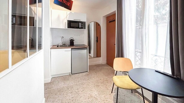 A compact kitchen with a microwave, kettle, and sink. There is a small dining area with a table and chairs. A TV is mounted on the wall above the kitchen. - David D Angers 42 - One Bedroom Apartment, Sleeps 3 (Paris)