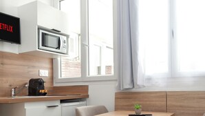 A compact kitchenette with a microwave, coffee maker, and a small sink. There is a dining area with a table and two chairs, and a window with curtains. - David D Angers 29 - One Bedroom Apartment, Sleeps 3 (Paris)